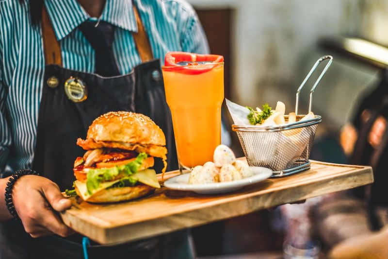 person serving burger with pitcher of juice