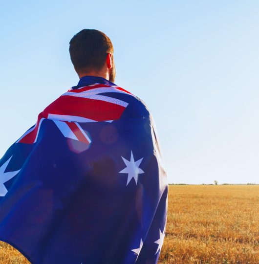 Man with a flag of Australia standing in morning field